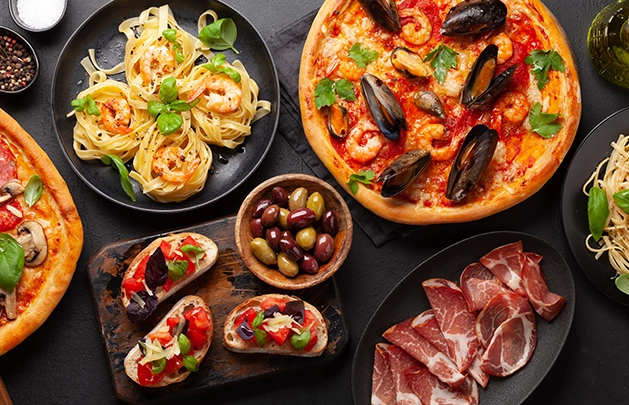 Table spread that has seafood pizza, seafood pasta, pepperoni pizza, plain pasta, olives, cured meats and bruschetta