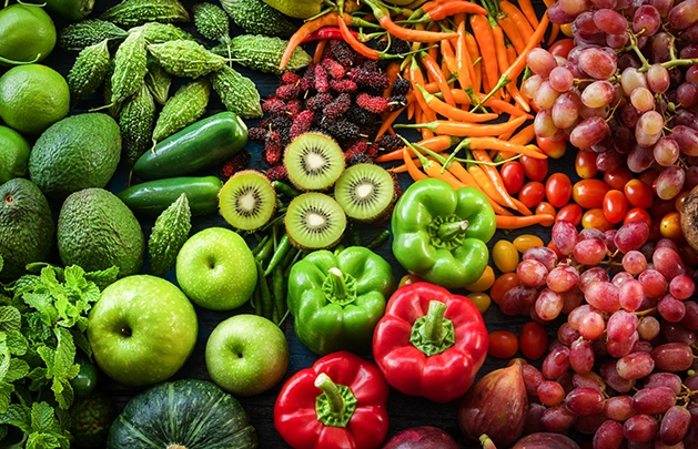 aerial view of fruits and vegetables next to one another Fruits include: limes, avocadoes, pumpkin, granny smith apples, green bell peppers, dragon berries, red bell peppers, spicy orange pepper, figs and red grapes